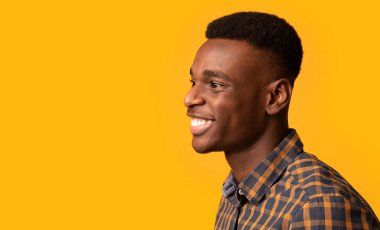 Bin yıllık neşeli Afro-Amerikan bir adamın yan görüntüsü sarı arka planda izole edilmiş, yakışıklı siyah bir adamın profil görüntüsü samimi bir şekilde gülümseyen ve başka yöne bakan, kopyalama alanı olan bir panorama.