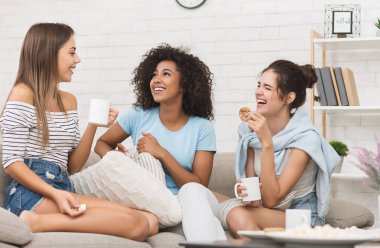 Mutlu oda arkadaşları kahve içiyor, sohbet ediyor ve evde gülüyor.