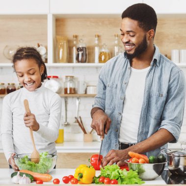 Tatlı afro kız ve babası taze salata pişiriyorlar. Birlikte vejetaryen yemekleri pişirmek