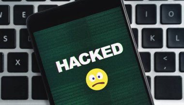 Sim-takas saldırı konsepti. Hacklenmiş yazı ve üzgün emoji simgesine sahip akıllı telefon dizüstü bilgisayarın klavye arka planında