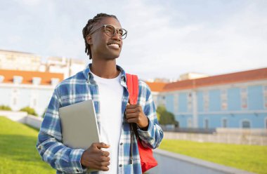 Çevrimiçi Eğitim Programları. Sırt çantalı ve dizüstü bilgisayarlı gülümseyen siyahi öğrenci üniversite kampüs binasının önünde dikiliyor, diğer tarafa bakıyor. E- Öğrenme Teklifi Konsepti için Boşluğu Kopyala