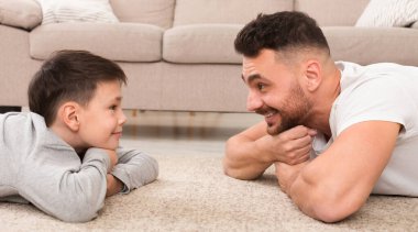 Evde kal. Tatlı çocuk ve yakışıklı adam birbirlerine bakıyorlar, evde yerde yatıyorlar, panorama