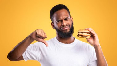 Abur cubur yeme. Burgerci Siyah Adam, Sarı Stüdyo Arkaplanında Ayakta Durarak İşaret Ediyor. Afrikalı Adam Sağlıksız Fast food 'u onaylamıyor. Kötü Beslenme alışkanlığı kavramı