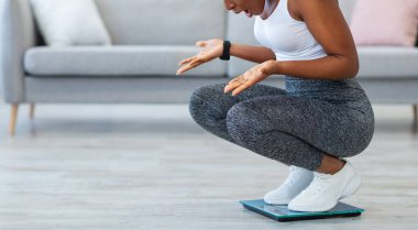 Kilo alma. Evde zayıf düştükten sonra tartıya çıkan siyahi kadın kendini tartıyor. Kadın Aşırı Kilo Alma Konsepti. Metin için Boşluk