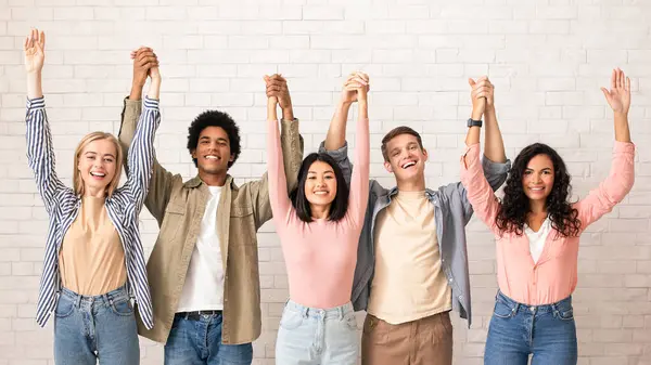 Takım çalışması, çalışmada bir arkadaştan destek ve başarı duyguları. Neşeli dijital genç uluslararası insanlar el ele tutuşup eğleniyorlar, beyaz duvar arkasında, stüdyo çekimlerinde, boş alanlarda.
