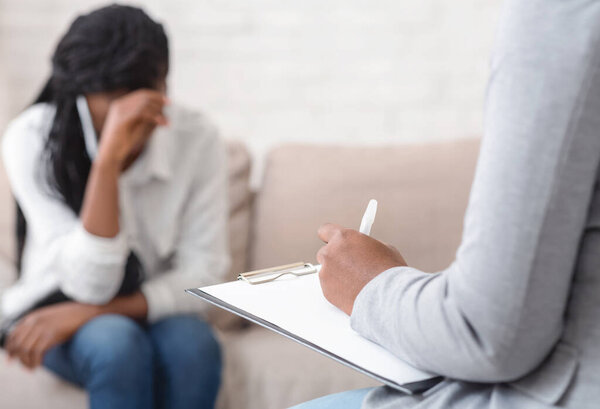 Unrecognizable female psychologist noting problems of woman patient at therapy session,selective focus