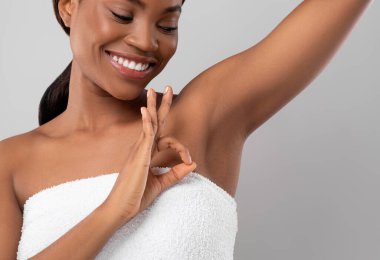 Güzel, genç, siyah kadın koltukaltını gösteriyor ve tamam jest yapıyor, mutlu Afrikalı Amerikalı kadın elini kaldırıyor, koltukaltı depolama sonucunun keyfini çıkarıyor, gri stüdyonun arka planında duruyor, kopyala