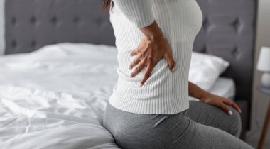 Halk ve Sağlık Sorunları Konsepti. Sol tarafta akut ağrıdan muzdarip hasta genç siyahi kadın kostümü, evde yatağında oturuyor, elleriyle sırtına dokunuyor, bedava fotokopi alanı.