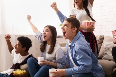 Televizyonda maç izleyip zaferi kutlayan fanatik futbol hayranları evde cips ve patlamış mısır yiyor.