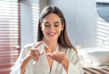 Yüzü temizlemek için pamuk yastığa hidrofilik yağ süren mutlu genç bir bayan. Gülümseyen güzel bir kadın banyoda günlük cilt bakımını yapıyor. Evde güzellik tedavisinden zevk alıyor.