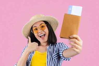 Pasaportu olan mutlu Asyalı kadın yolcu portresi uçak biletleri ve güneş gözlüğü takan, yaz şapkası takan, günlük kıyafetler giyen pembe stüdyo duvarı olan.