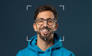 Gözlüklü neşeli bir adam mavi bir kapüşonlu giyerken gülümsüyor, yüzünü kaplayan yüz tanıma çizgileri olan karanlık bir arkaplan üzerine kurulmuş..