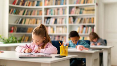 İlkokuldaki sınıfların masalarında oturan, not defterine yazı yazan ya da resim çizen bir grup öğrenci. Tekrar açılıyor ve okula geri dönüyor.