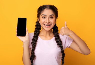 Tavsiye ederim. Elinde siyah bir ekranla akıllı telefonu tutan heyecanlı Hintli genç bir kadının portresi. Cihazı ve işaret işaretini gösteriyor. Model için boş boş alanı olan Gadget