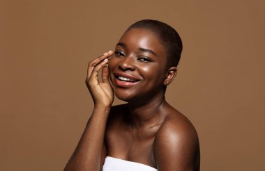 Temel Güzellik. Temiz tenli, kısa saçlı, kameraya gülümseyen çekici siyahi kadın portresi, kahverengi arka planda güzel Afro-Amerikan kadın posu, kopyalama alanı.