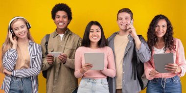 Modern cihazlar, yaşam tarzı ve yurtdışındaki öğrenciler. Modern cihazlarla gülümseyen çok ırklı genç insanlar, müzik dinliyorlar, mesaj yolluyorlar, okuyorlar ve internette sörf yapıyorlar turuncu arka planda izole olmuşlar.