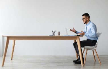 Video konferansı. Profil yan görüntüsü Orta Doğulu iş adamının gözlüklü portresi web araması yapıyor, bilgisayarını kullanıyor, iş yerinde oturuyor, konuşuyor ve webcam 'da el kol hareketi yapıyor, ücretsiz fotokopi alanı afişi