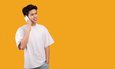 Her zaman temastayız. Akıllı telefonuyla konuşan sıradan gülümseyen Asyalı adamın portresi, fotokopi alanına bakıyor, turuncu stüdyo arka planında izole bir şekilde duruyor ve poz veriyor, afiş. İletişim, Telefon Çağrısı