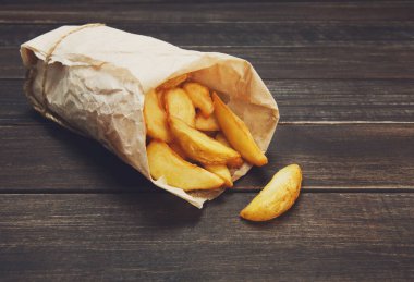 Kahverengi kraft ambalaj kağıdına sarılmış lezzetli patates dilimleri. Fast food alır. Rustik ahşap tahtalar arka planda kızarmış patates. Ağaçta patates. Kızarmış cips, patates dilimleri. Üst görünüm, yumuşak ton