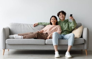 Ev içi boş zaman aktiviteleri. Olumlu genç Asyalı çift kanepede dinleniyor, TV seyrediyor, uzaktan kumandayla kanal değiştiriyor, evde birlikte filmden zevk alıyorlar, bedava uzay.