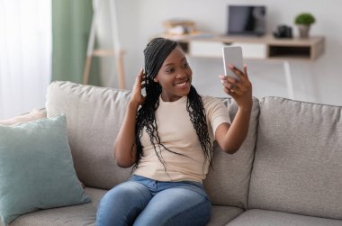 Zarif rastaları olan, sosyal medya ya da arkadaşlar için akıllı telefondan selfie çeken hoş, genç siyahi bir bayan. Afro-Amerikalı bir kadın evde eğleniyor, cep telefonu kullanıyor, uzay kopyaları yapıyor.