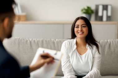 Başarılı psikoterapi. Mutlu Arap kadın müvekkil psikologla seans yapıyor, gülümsüyor, klinikte kanepede oturuyor. Olumlu kadın terapistle iletişim kuruyor, duygusal sorunları çözüyordu.