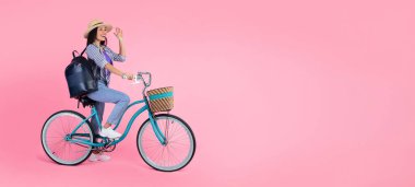 Merhaba Summer. Hasır şapkalı ve sırt çantalı gülümseyen Asyalı kadın profili. Klasik bisiklete biniyor. Pembe stüdyo duvarında, afişte ve panoramada izole edilmiş bedava fotokopi alanına el sallıyor.