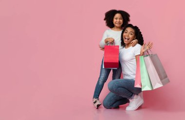 Alışveriş eğlencesi. Neşeli Afrika kökenli Amerikalı anne ve kız, kâğıt alışverişi torbalarıyla poz veriyor, Pembe arka planda kucaklaşıyor, Boşluğu kopyalıyor.