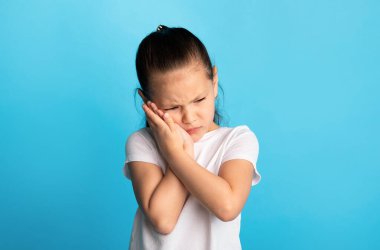 Diş Duyarlılığı Konsepti. Mutsuz Asyalı kız diş ağrısı çekiyor. Dokunaklı yanak, mavi stüdyo duvarı, fotokopi odası.