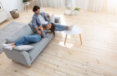 Mutlu çift hafta sonunu birlikte geçiriyor, erkek kahve içiyor, kadın kanepeye uzanıyor ve telefon, yan görüş, boş alan kullanıyor.