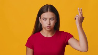 Uzun kahverengi saçlı genç bir kadın ciddi bir ifadeyle doğrudan kameraya bakıyor. Onun odaklanmış bakışları parlak turuncu bir arka plana karşı, onun özelliklerini vurguluyor.