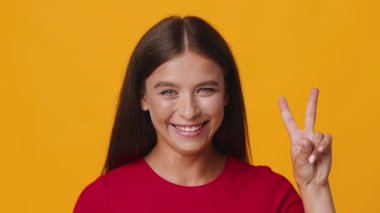 Genç beyaz bir kadın parlak sarı bir arka fonun önünde duruyor, eli çenesinde, düşünceli bir şekilde bakıyor. İfadesi derin düşüncelere ve meraka işaret ediyor..