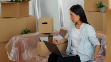 Çinli kadın kutularla çevrili yeni bir daireye taşınmaya hazırlanıyor. Dizüstü bilgisayarında çalışan bir kadın, taşınma detaylarını yönetirken bir yandan da içki içiyor..