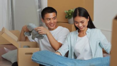 Genç bir çift, yeni dairelerine taşınmaya hazırlanırken kıyafetlerini ve eşyalarını kutulara koymaktan mutluluk duyuyorlar. Bu heyecan verici yer değiştirme döneminde gülücüklerini paylaşıyorlar..