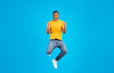 Zaferin sevinci. Duygusal siyahi adam evet diyor ve mavi arka planda havadan poz veriyor. Milenyum Adamı Atlıyor ve Titreyen Yumruklar Stüdyoda Başarıyı Kutlayan Kameraya Bakıyor