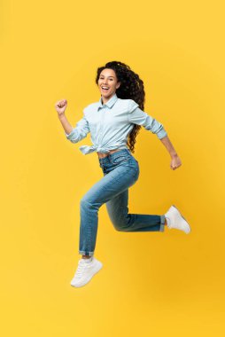 Evet, harika haberlerim var. Heyecanlı genç bayan yüksekten atlıyor, zaferi veya zaferi kutluyor turuncu sarı stüdyo arka planında izole edilmiş kameraya bakıyor, tüm vücut uzunluğu dikey afiş.