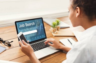 İş Arama Konsepti. Cep telefonu tutan siyah kızın omzunun üstünden bak, ekranda boş internet sitesi olan bir laptop kullan