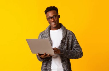 Joy 'la çalışmak. Yakışıklı genç Afrikalı adam dizüstü bilgisayar kullanıyor ve sarı arka planda gülümsüyor.