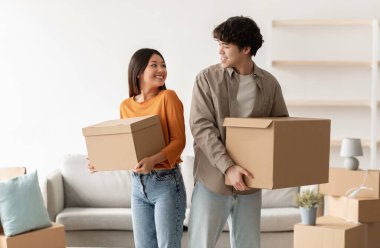 Ev taşıma konsepti. Pozitif genç Asyalı çift, kendi evlerinde kutu taşıyorlar. Yeni mülke taşınan bin yıllık kiracıların portresi.