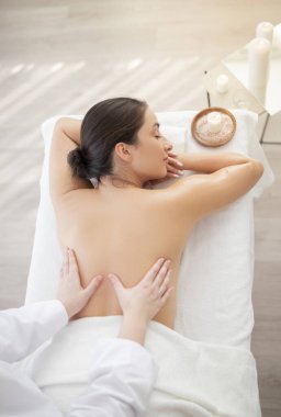 Spa salonunda sırt masajından hoşlanan rahat Hintli bir kadın. Profesyonel kadın terapistin, sağlık merkezinde genç ve çekici bir bayana terapi uygulamasının en iyi görüntüsü.