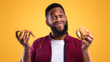 Abur cubur yiyen. Burger ve Pizzanın Dilimi Sarı Stüdyo Arkaplanında Duruyor. Sağlıksız Beslenme, Aldatma Yemeği ve Fast food Aşırı Yeme Sorunu, Aşırı Yeme Alışkanlığı