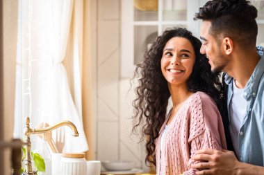 O mutfakta bulaşık yıkarken, Arap kocasını seven, karısını arkadan kucaklayan, evde birbiriyle kaynaşan orta doğulu bir aile, boş alanla kenar manzaralı bir aile.