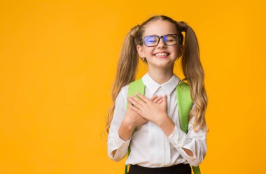 Teşekkürler konsept. Minnettar bir ilkokul öğrencisi sarı stüdyo arka planında gözleri kapalı ellerini göğsüne koyuyor. Kopyalama alanı