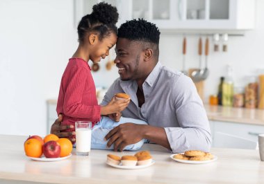 Mutlu, genç, siyah bir baba, gülümseyen küçük kızına sarılıyor, birlikte yemek yerken mutfakta kaynaşıyor, kız masaya oturuyor, kek tutuyor, süt içiyor, fotokopi çekiyor. Babalık kavramı