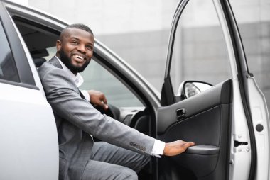 Yakışıklı siyahi iş adamı arabadan çıkıyor, bir yerlere bakıyor ve gülümsüyor, yeni iş günü için heyecanlanıyor. Mutlu Afrikalı Amerikalı girişimci ofise geldi, otomobili terk etti.