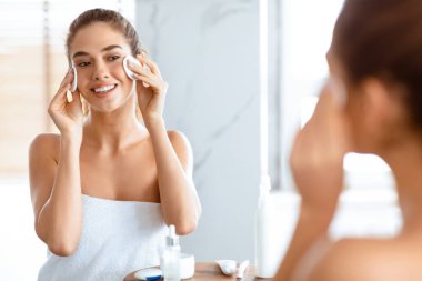 Yüz bakımı. Pamuk pedli Mutlu Kadın Temizleme Yüzü. Tuvalette aynanın yanında duran makyajı kaldırıyor. Dişi cilt bakımı ve güzellik rutini. Seçici Odaklanma