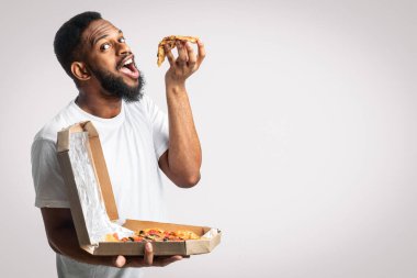 Sakallı, pizza yiyen, beyaz stüdyo arka planında büyük bir pizza kutusu olan siyah adam. Abur cubur yiyici Fast food 'un tadını çıkarıyor. Sağlıksız Erkek Beslenme ve Aşırı Yeme