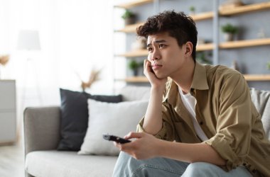 Sıkıcı Televizyon Programı. Sıkıcı Asyalı adam TV izliyor uzaktan kumandayla kanal değiştiriyor evdeki koltukta oturuyor. Hoşnutsuz İzleyici İlginç Olmayan Film İzliyor, Yalnız Hissediyor