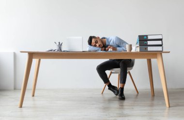 Enerji Konsepti eksikliği. Yorgun Orta Doğulu genç bir adamın iş yerinde uyuması, yorgunluktan bitap düşmüş bir adamın bilgisayar başında uyuyakalması, yorgun bir erkek işçinin dinlenmesi.