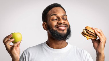 Siyah Adam Burger ve Elma 'nın Sağlıklı ve Sağlıksız Yiyecekler Stüdyoda Beklerken Beyaz Arkaplanda Seçimi. Erkek Beslenme ve Önemsiz Yiyecekler, Diyet Konseptinde Aldatma Yemeği